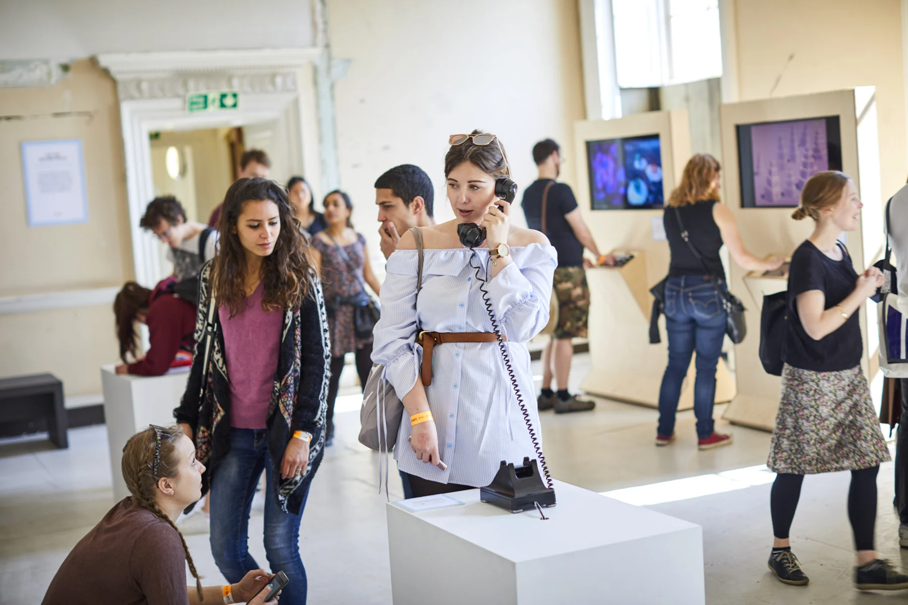 Visitors gather around a telephone on a white plinth.