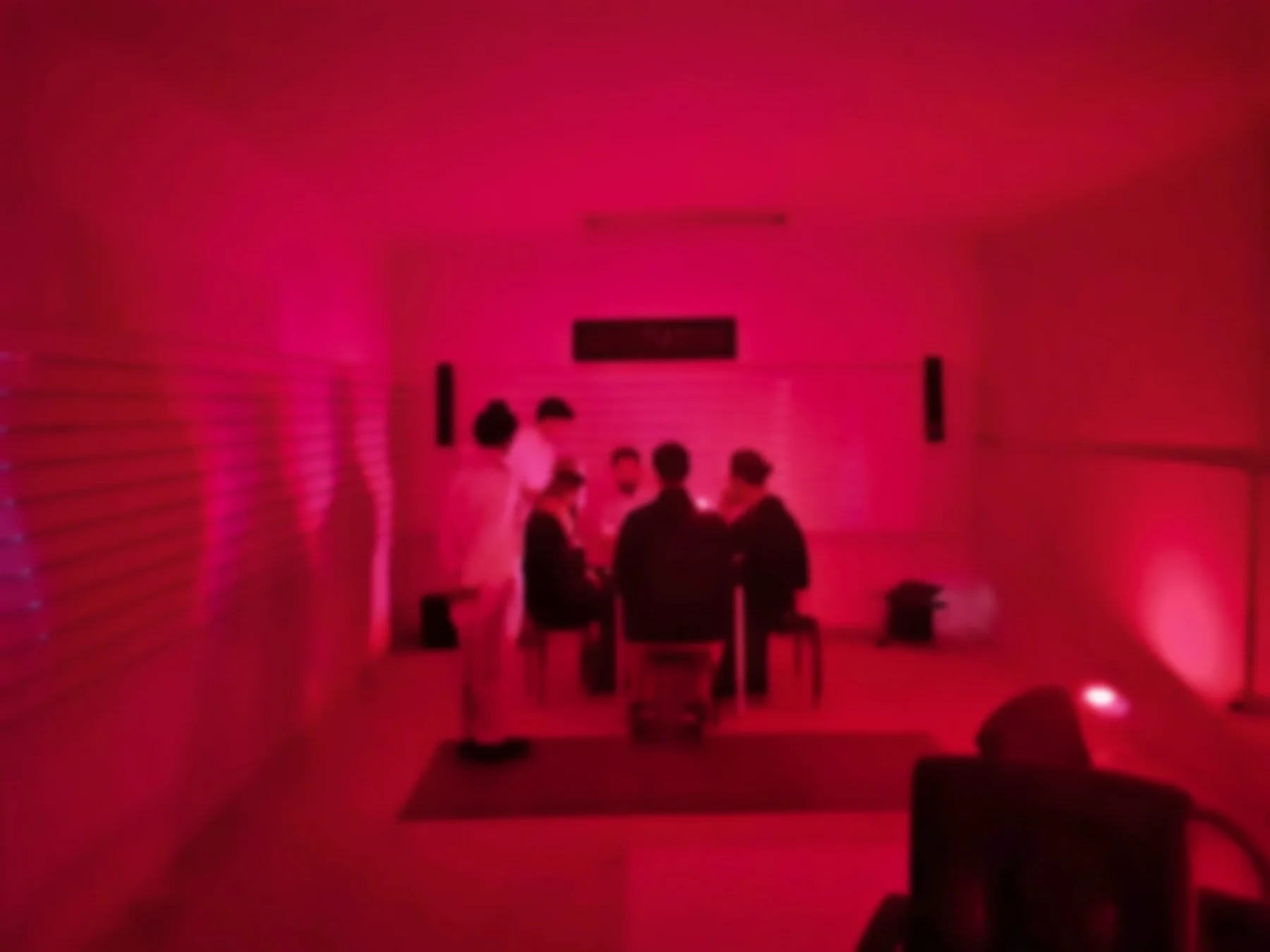 People at a table in the red-lit Gameshow set.