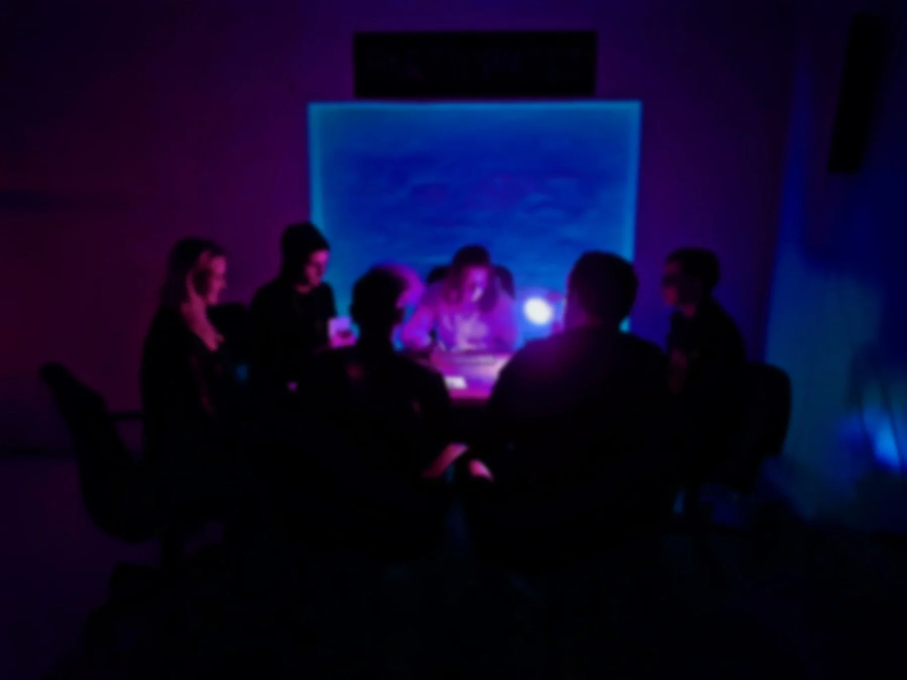 Players around a table beneath purple lights.