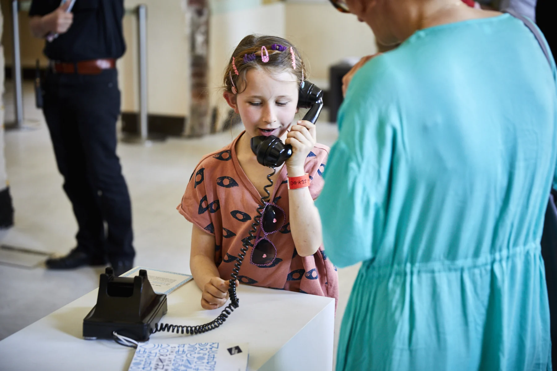 A child holding the telephone receiver and looking towards an adult.